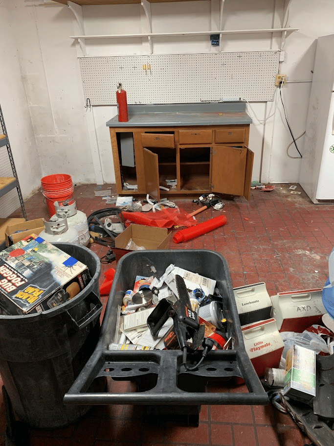 Garage workspace with tools, containers, and mixed household items staged for removal