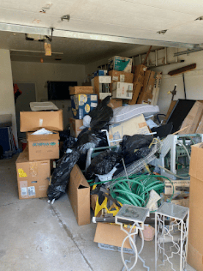 Cluttered garage filled with boxes, scrap materials, and household junk before cleanup by Pure Disposal